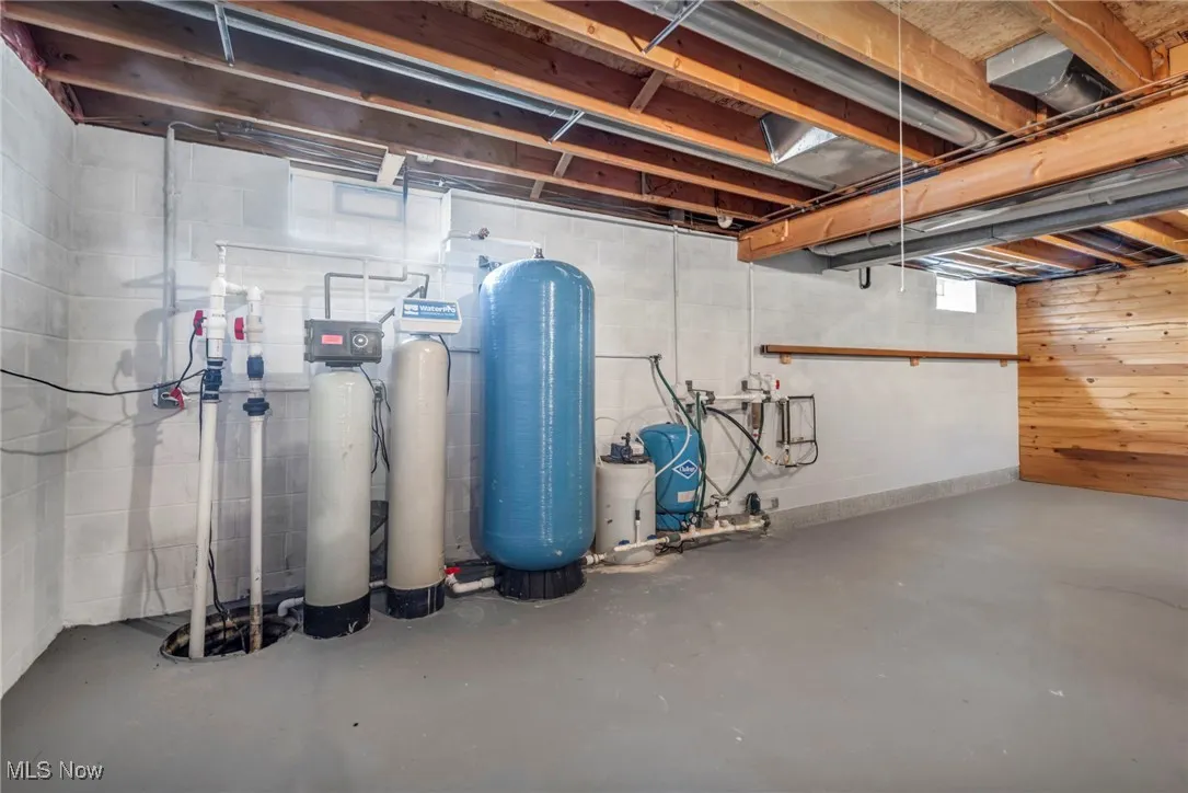 Below grade area featuring concrete block wall, a water pressure tank, drainage system, and a water softener system