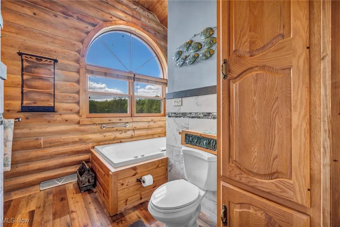 Bathroom with toilet, hardwood / wood-style floors, and rustic walls