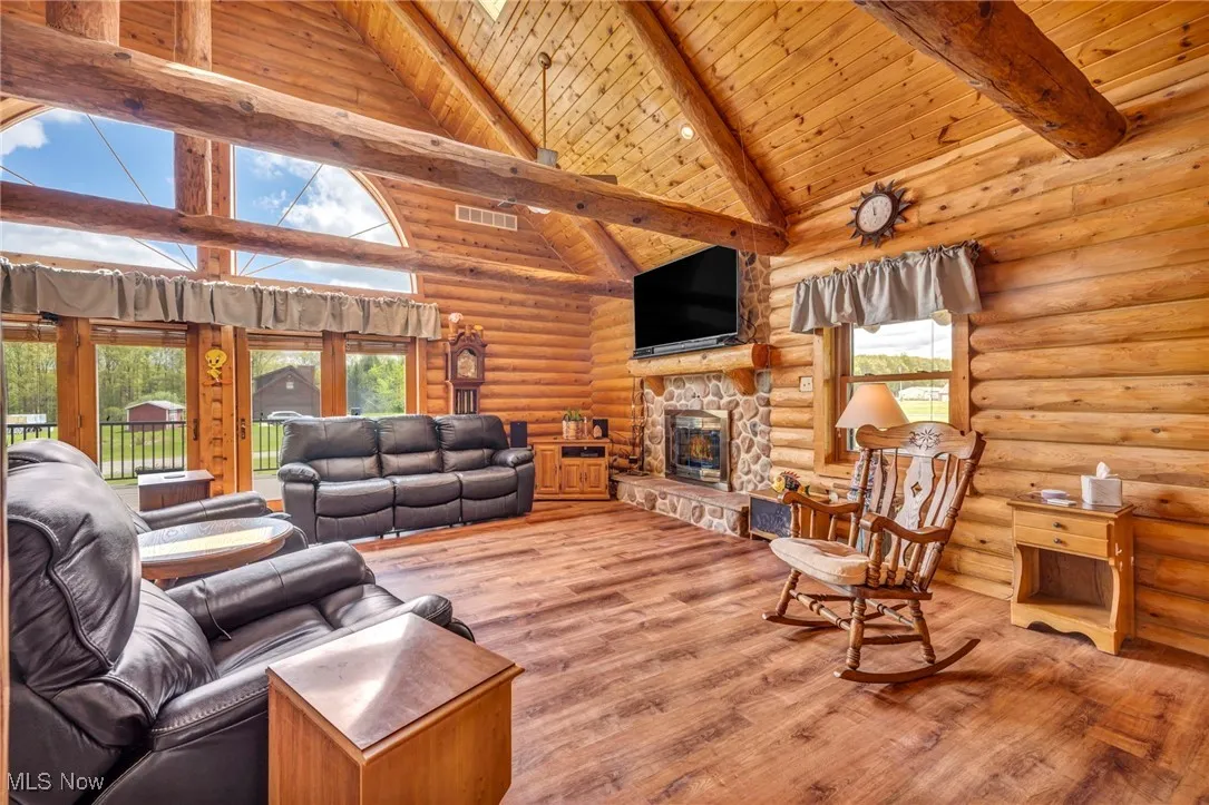 Living room with log walls, beam ceiling, wooden ceiling, wood finished floors, and a fireplace