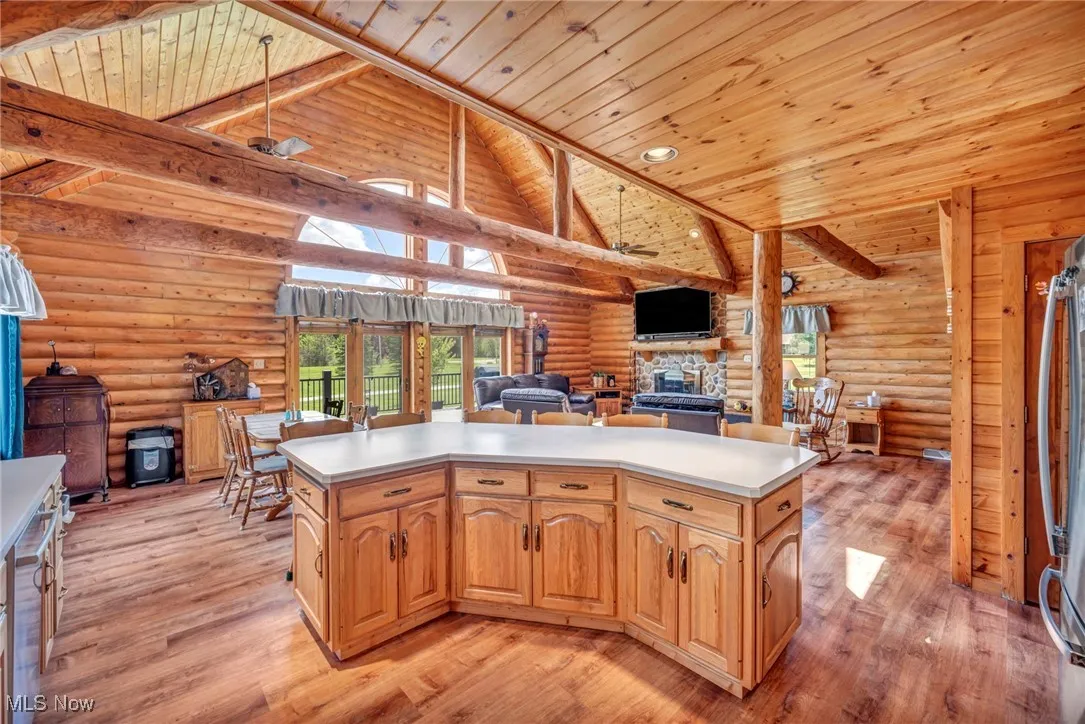 Kitchen featuring open floor plan, a fireplace, light wood finished floors, log walls, and wood ceiling