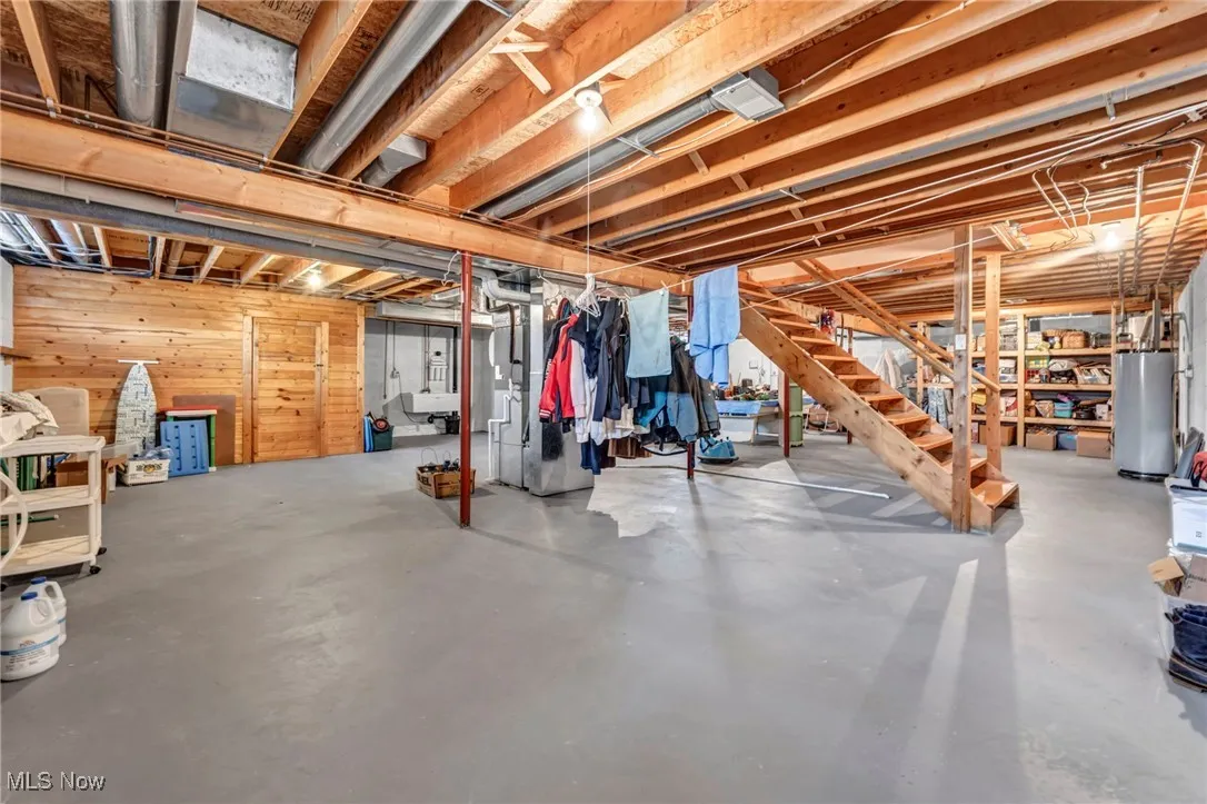 Unfinished basement featuring water heater, stairs, and wooden walls