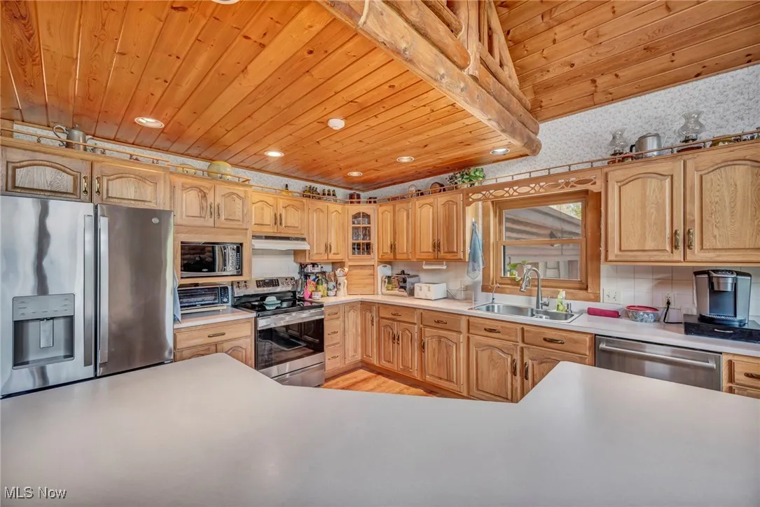 Kitchen featuring stainless steel appliances, wood ceiling, a sink, light countertops, and under cabinet range hood