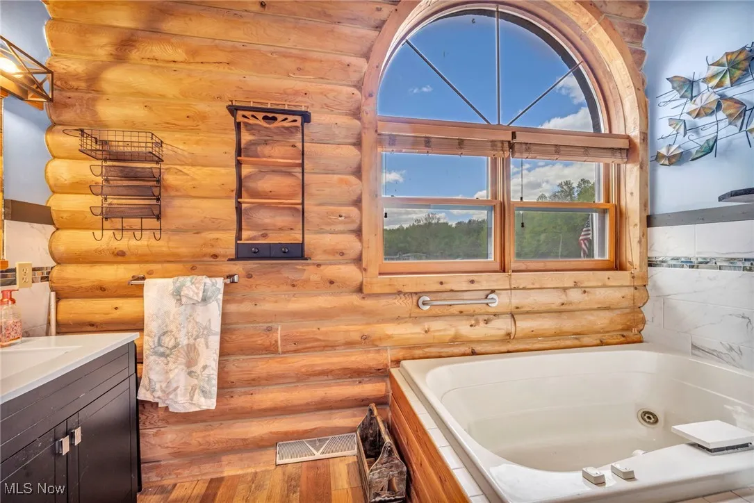 Full bath with log walls, wood finished floors, a whirlpool tub, and vanity