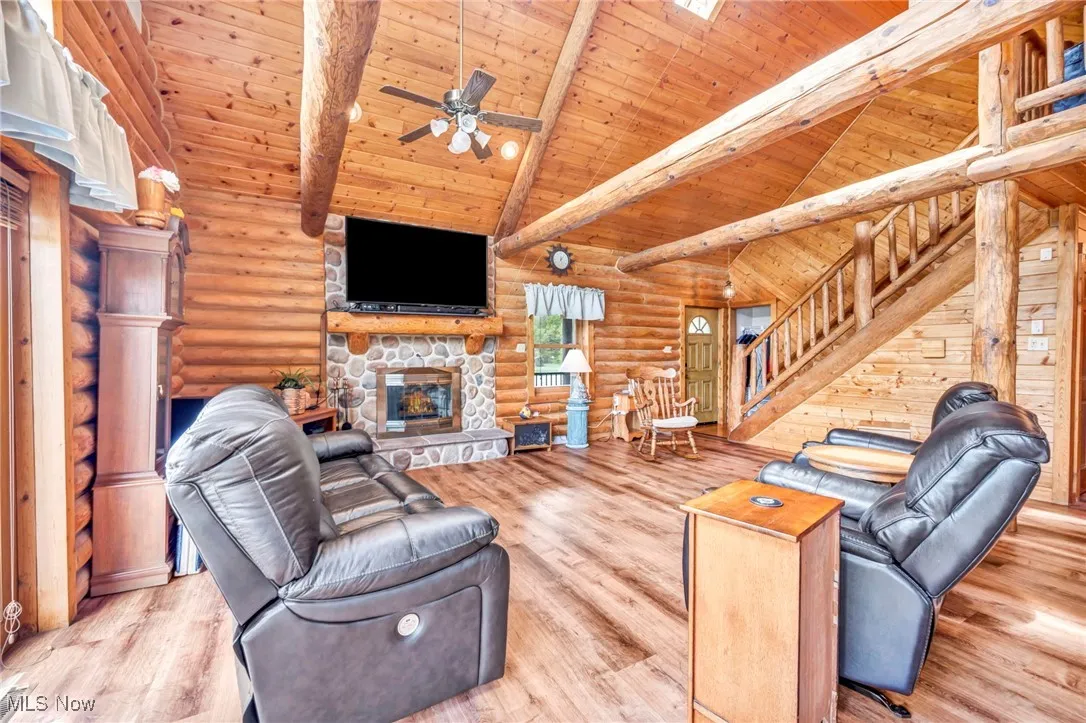 Living area featuring log walls, stairs, wood ceiling, a fireplace, and wood finished floors