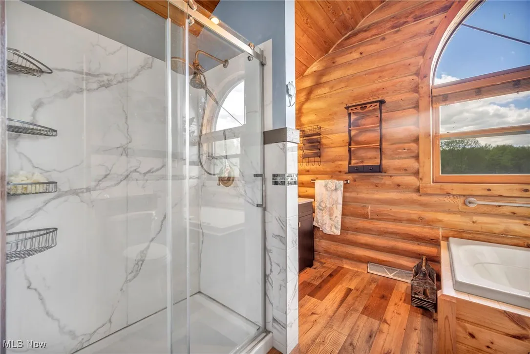 Bathroom featuring log walls, hardwood / wood-style flooring, a marble finish shower, vanity, and vaulted ceiling