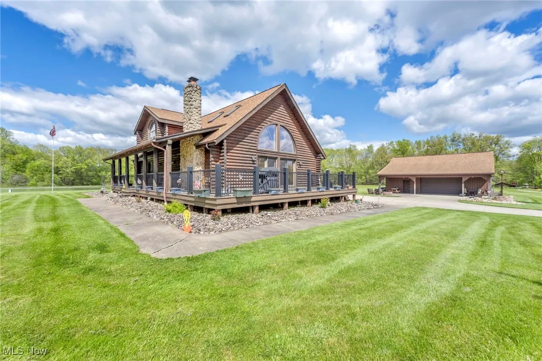 Side view of house featuring log siding, a chimney, a yard, a deck, and a detached garage