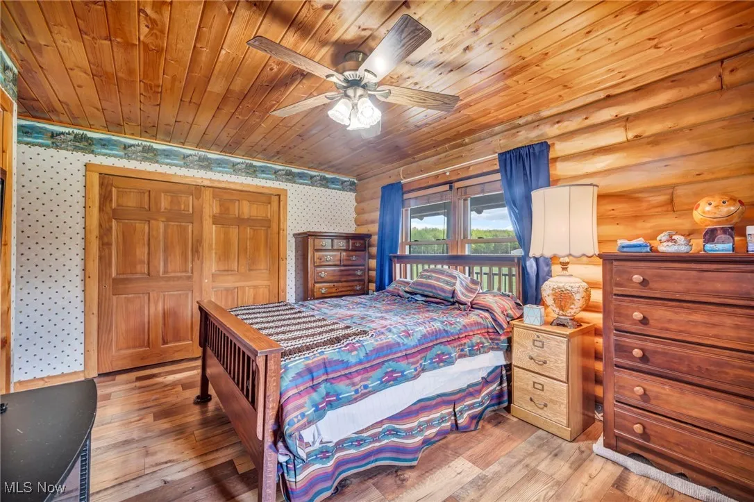 Main floor bedroom with wood ceiling, light wood finished floors, rustic walls, and ceiling fan