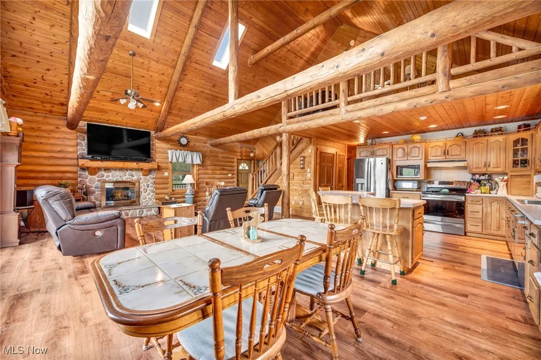 Dining room featuring wood ceiling, a fireplace, high vaulted ceiling, rustic walls, and a skylight