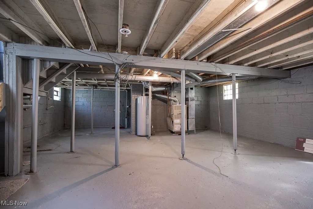 Basement with electric water heater, heating unit, and healthy amount of natural light
