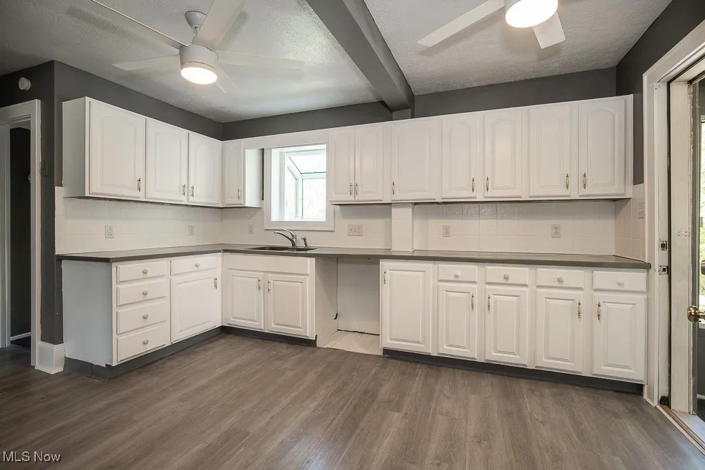 Kitchen with a ceiling fan, a sink, beam ceiling, tasteful backsplash, and white cabinets