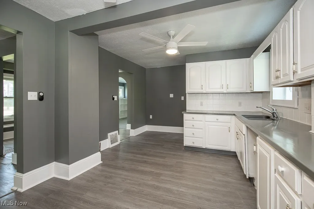 Kitchen featuring a sink, a ceiling fan, white cabinetry, decorative backsplash, and a textured ceiling