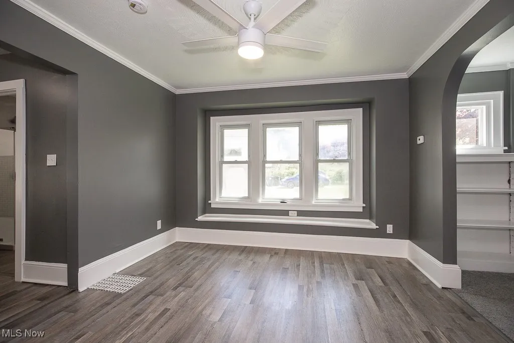 Dining room with arched walkways, dark wood-type flooring, a ceiling fan, baseboards, and crown molding