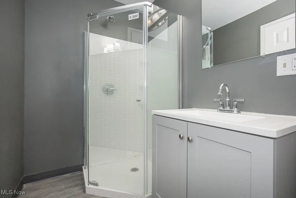 Bathroom on first floor featuring a shower stall, wood finished floors, vanity, and baseboards