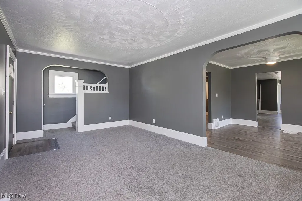 Carpeted living room featuring arched walkways, a textured ceiling, baseboards, crown molding, and stairs