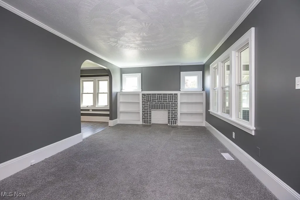 Unfurnished living room with carpet flooring, a textured ceiling, crown molding, a fireplace with flush hearth, and baseboards