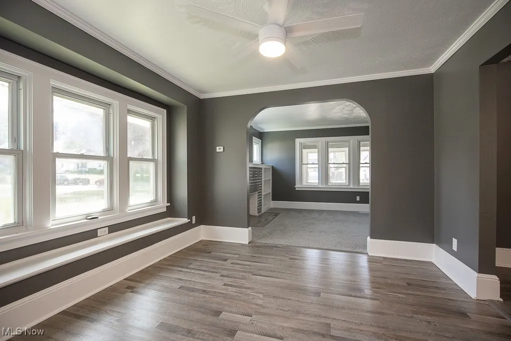 Empty dining room with arched walkways, baseboards, wood finished floors, crown molding, and a ceiling fan