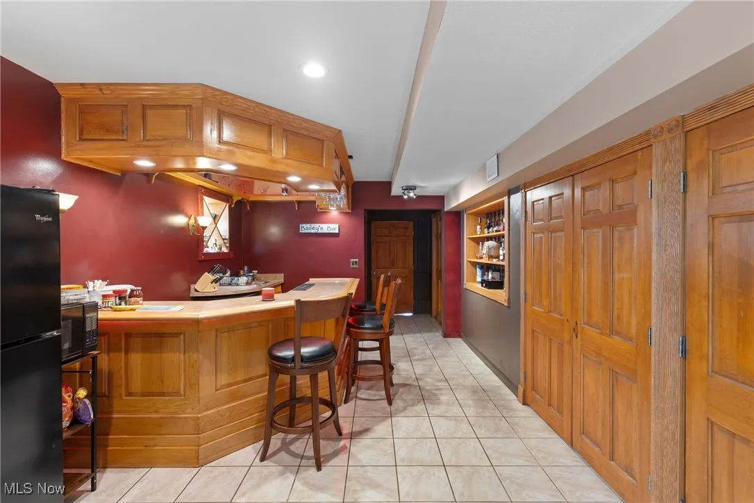 Indoor bar with black appliances, light tile patterned flooring, recessed lighting, and built in features