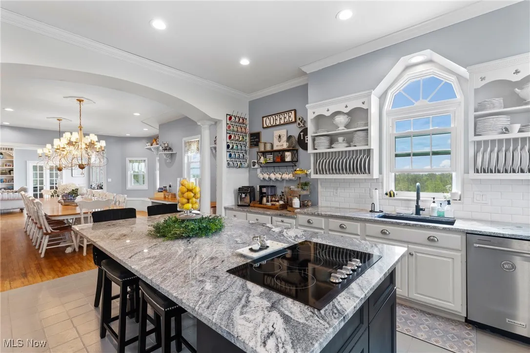 Kitchen with dishwasher, black electric stovetop, decorative columns, a sink, and arched walkways