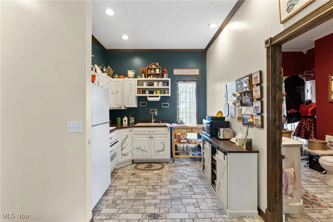 Kitchen with white cabinets, dark countertops, open shelves, a sink, and crown molding