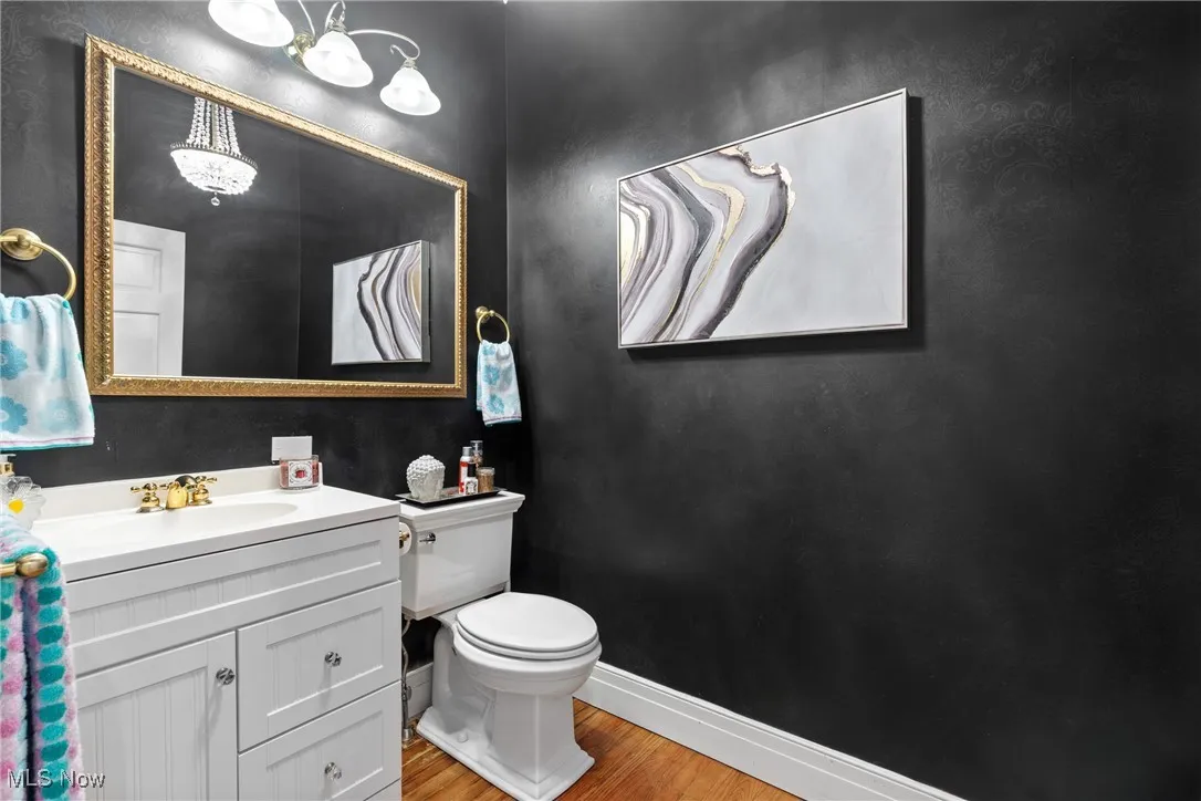 Half bath featuring wood finished floors, baseboards, toilet, vanity, and a chandelier