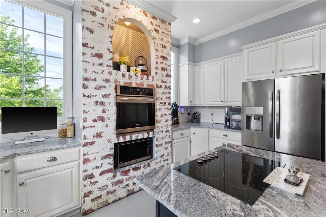 Kitchen featuring appliances with stainless steel finishes, plenty of natural light, white cabinets, tile patterned flooring, and ornamental molding
