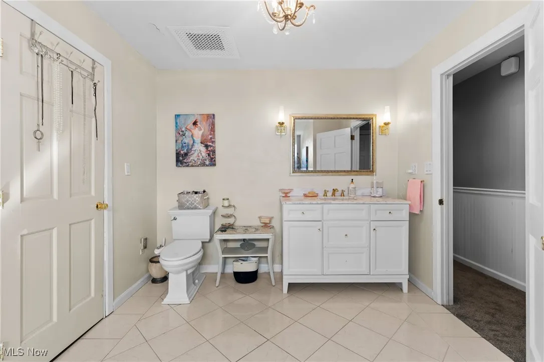 Bathroom featuring toilet, vanity, tile patterned flooring, and a wainscoted wall