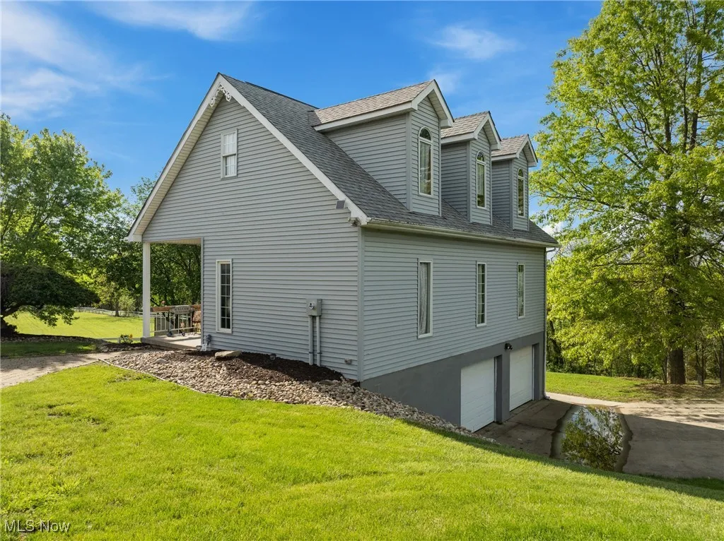 View of side of property with a shingled roof, an attached garage, a yard, and driveway