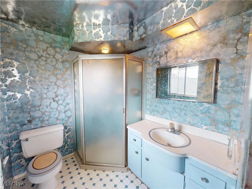 Full bathroom with wallpapered walls, a stall shower, toilet, and vanity
