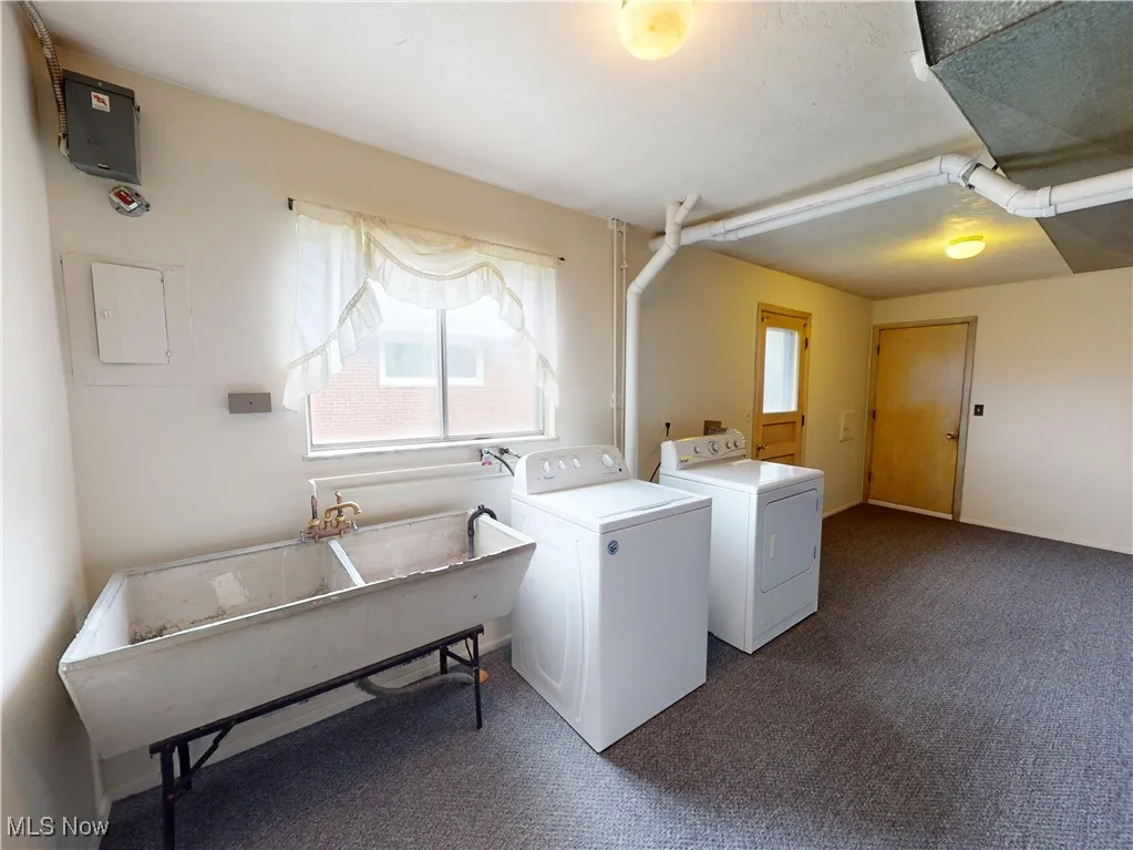 Clothes washing area featuring washer and dryer, dark carpet, electric panel, and baseboards