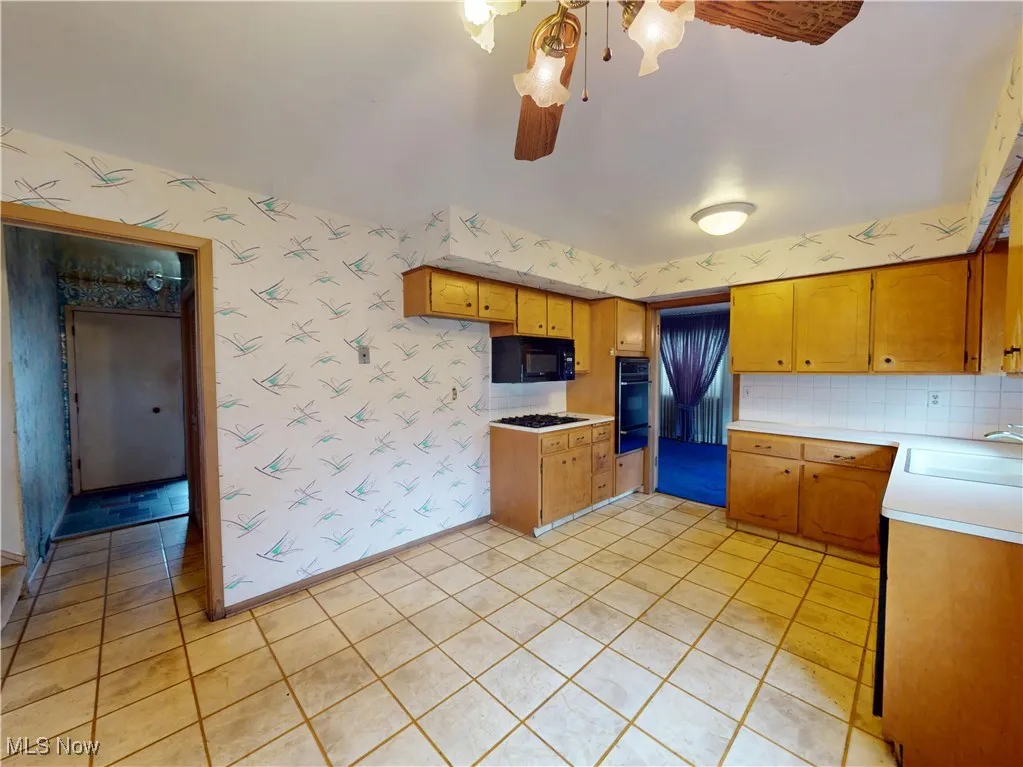 Kitchen featuring black appliances, a sink, wallpapered walls, light countertops, and ceiling fan