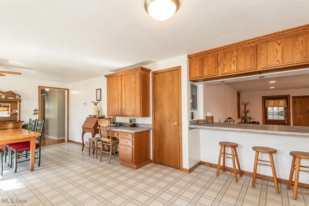 Kitchen featuring brown cabinets, light countertops, baseboards, a breakfast bar, and a ceiling fan