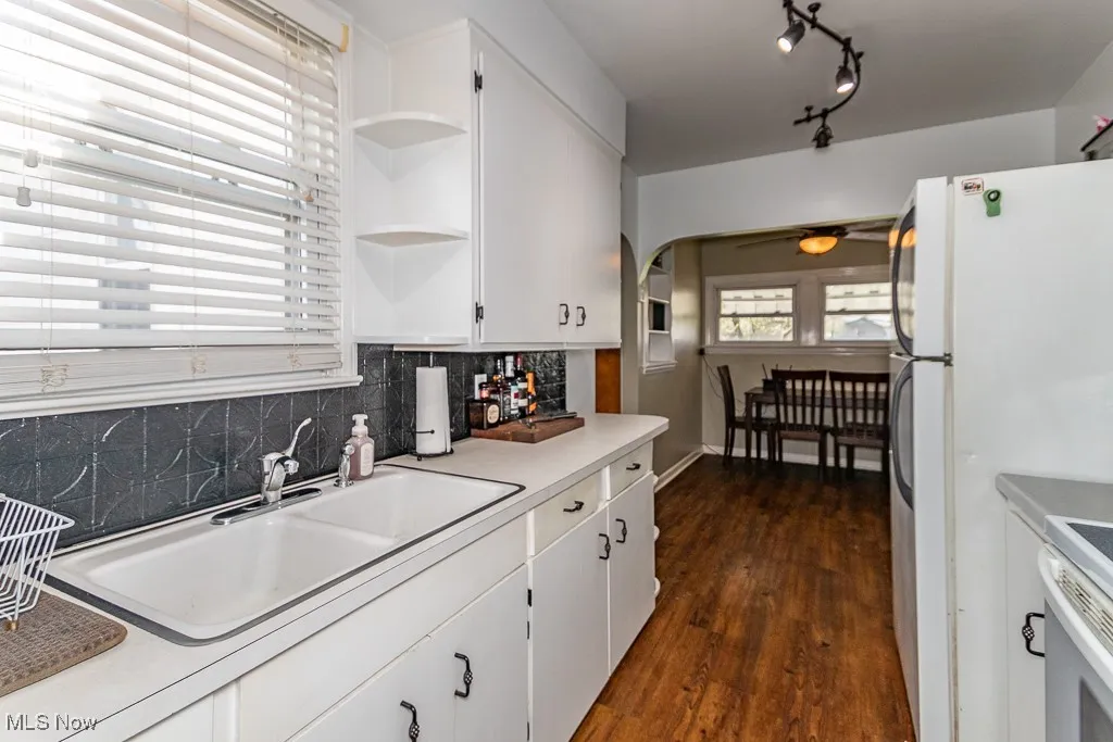 Kitchen featuring a sink, arched walkways, open shelves, dark wood-style flooring, and tasteful backsplash