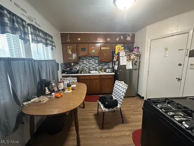 Kitchen with freestanding refrigerator, black gas range oven, light wood-style floors, a sink, and light countertops