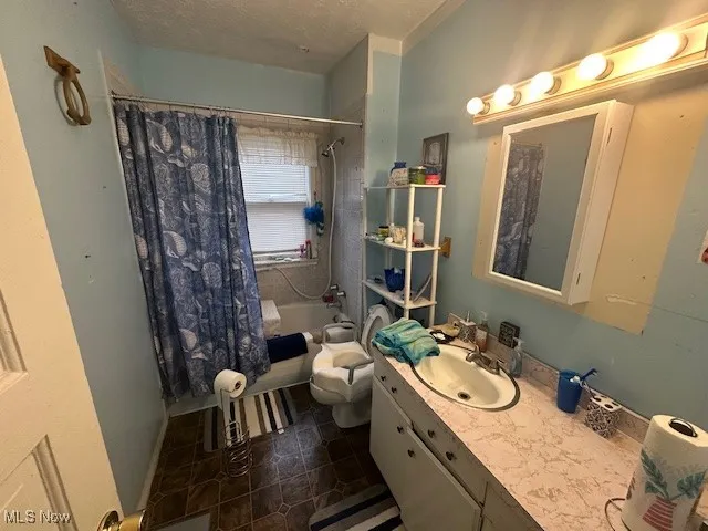 Bathroom featuring shower / tub combo with curtain, vanity, toilet, a textured ceiling, and tile patterned floors