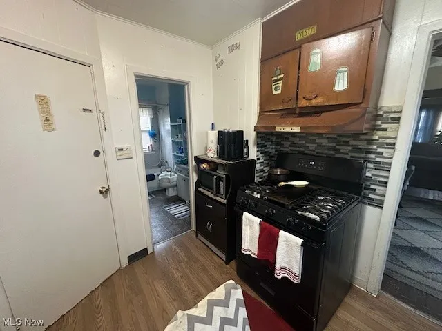 Kitchen with black appliances, under cabinet range hood, dark wood-style flooring, ornamental molding, and decorative backsplash