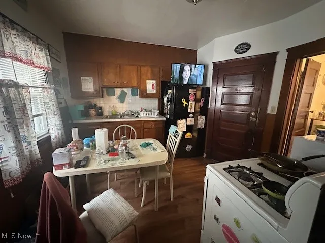 Kitchen featuring freestanding refrigerator, white range with gas stovetop, dark wood-style flooring, brown cabinets, and a sink