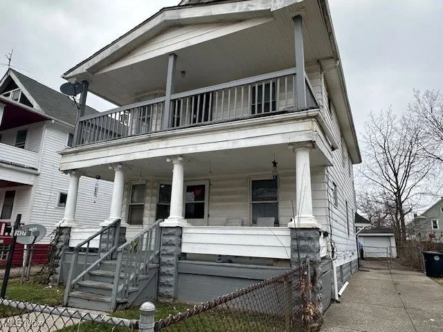View of front of property featuring a porch, fence, an outdoor structure, and a balcony