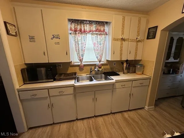 Kitchen with a sink, light wood-style flooring, black microwave, light countertops, and a textured ceiling