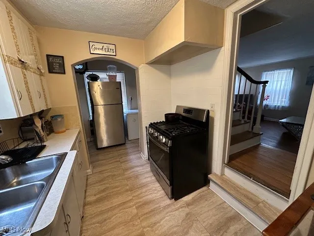 Kitchen featuring stainless steel range with gas stovetop, freestanding refrigerator, a sink, light countertops, and a textured ceiling