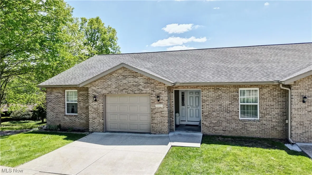 Single story home featuring a garage, roof with shingles, a front lawn, concrete driveway, and brick siding