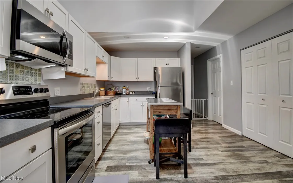Kitchen with appliances with stainless steel finishes, white cabinetry, light wood-type flooring, tasteful backsplash, and a sink