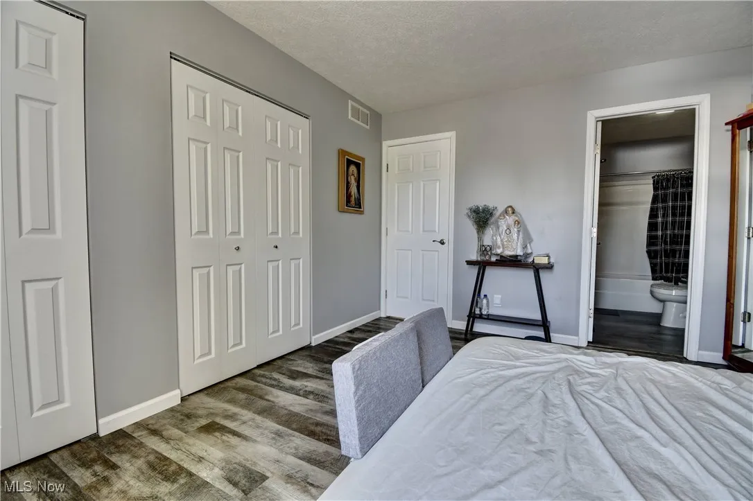 Bedroom with wood finished floors, baseboards, a textured ceiling, and connected bathroom