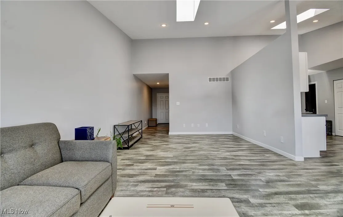Living room with a skylight, wood finished floors, baseboards, recessed lighting, and a high ceiling