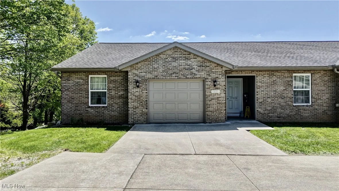 View of front of house featuring a shingled roof, an attached garage, brick siding, concrete driveway, and a front yard