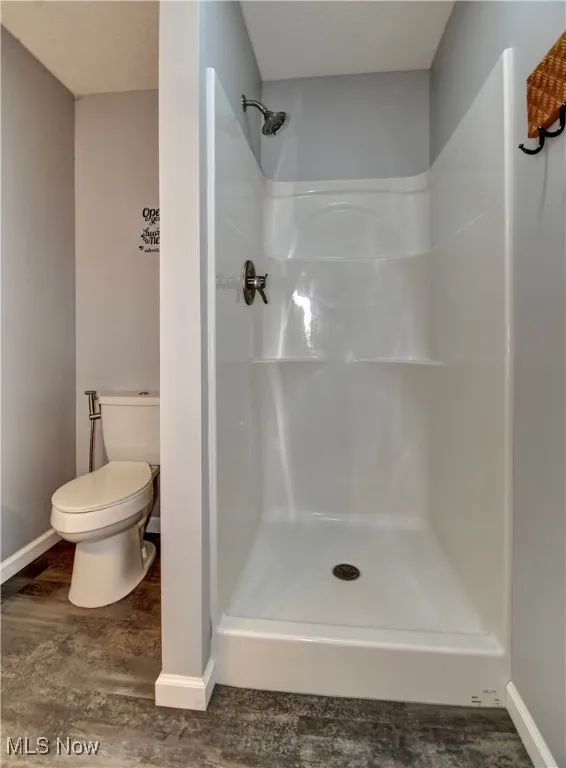 Full bathroom featuring a stall shower, toilet, baseboards, and wood finished floors