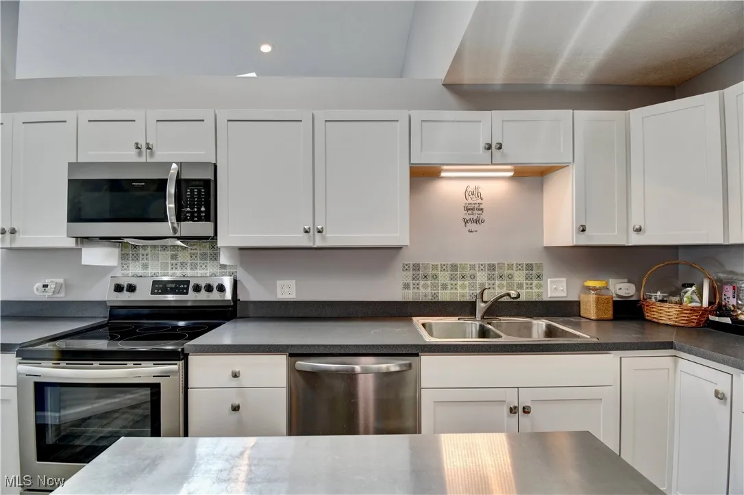 Kitchen featuring stainless steel appliances, a sink, dark countertops, white cabinetry, and recessed lighting