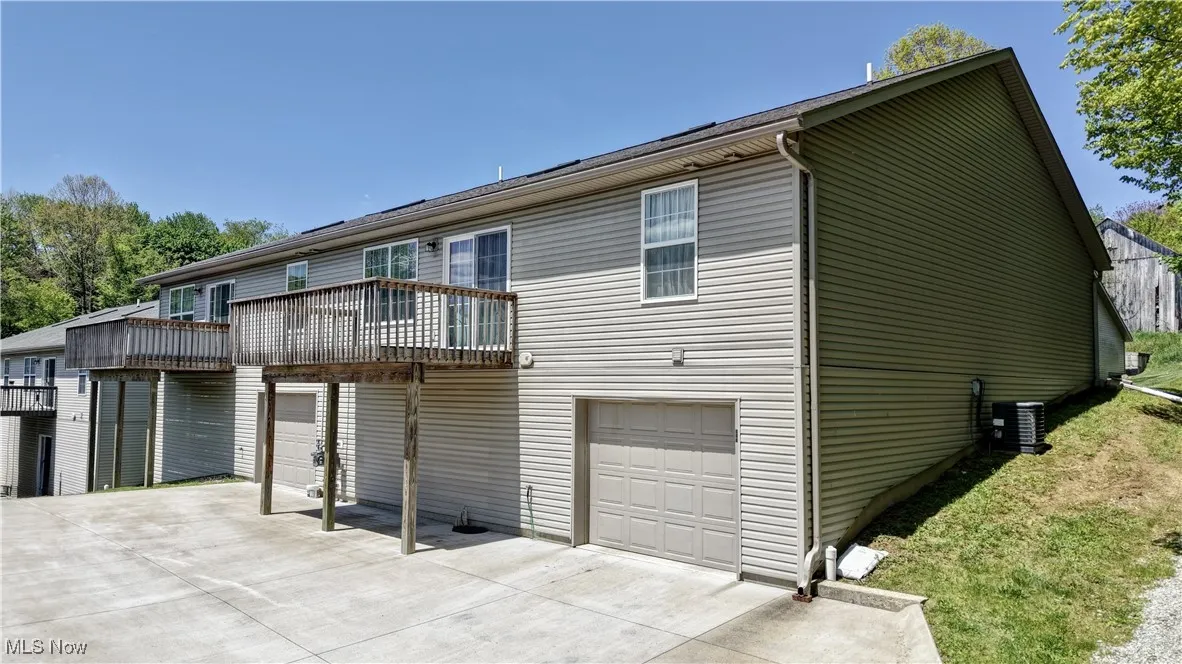 View of front of property featuring a garage, a balcony, concrete driveway, and central air condition unit