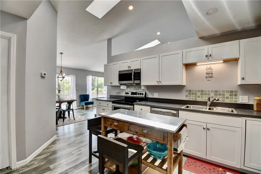 Kitchen with a sink, stainless steel appliances, dark countertops, a skylight, and tasteful backsplash