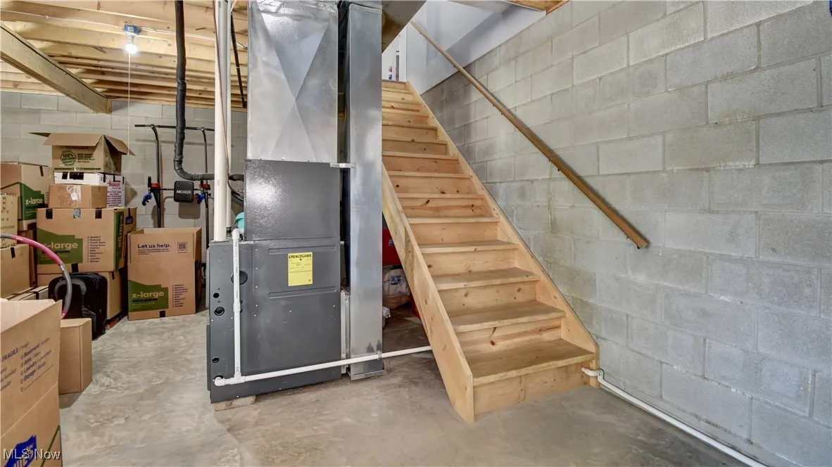 Unfinished basement featuring concrete block wall, stairway, and heating unit