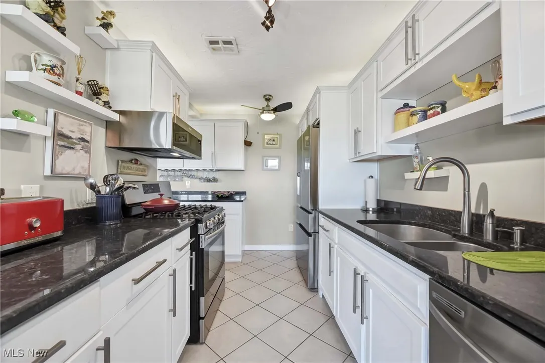 Kitchen featuring open shelves, appliances with stainless steel finishes, a sink, light tile patterned floors, and white cabinets
